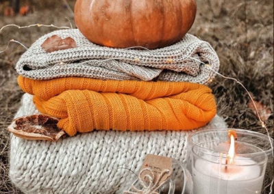 Stack of fall sweaters with pumpkin on top, next to a candle