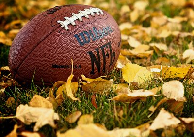 An American football resting on a field with yellow leaves