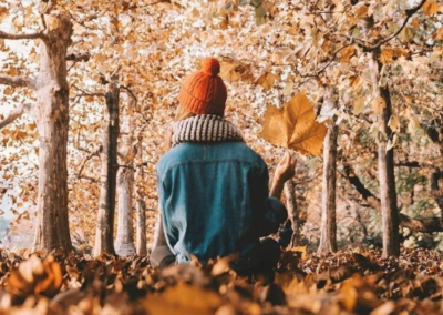 Girl with orange hat holding a big leaf sitting in a forest of fallen leaves