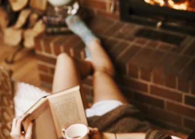 Girl reading a book near a fireplace, with a hot drink