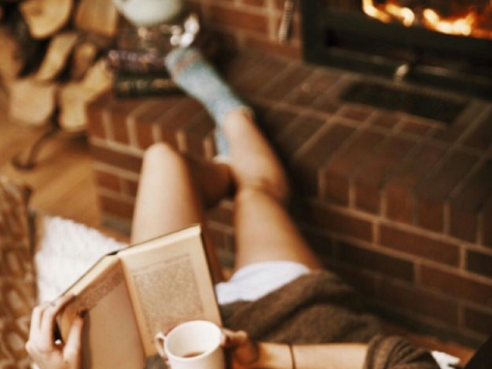 Girl reading a book near a fireplace, with a hot drink