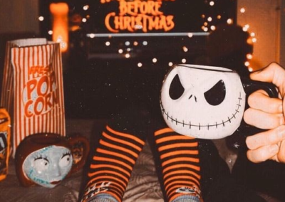 Person holding a skeleton mug with a movie on a TV in the background