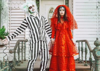 Two adults in Halloween costumes, one in Beetlejuice the other in red