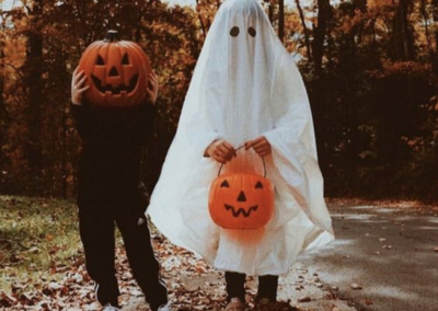 A kid with a pumpkin head standing next to a kid dressed as a ghost