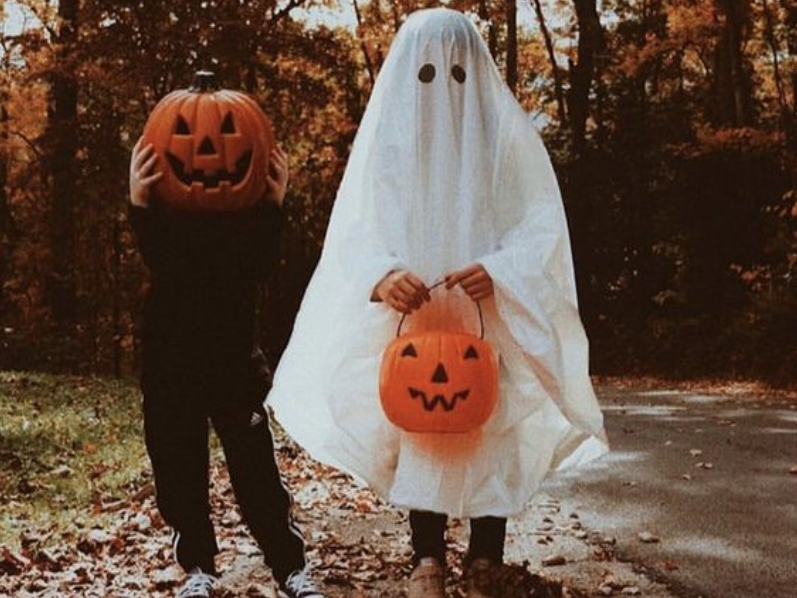 A kid with a pumpkin head standing next to a kid dressed as a ghost