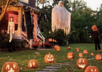 Halloween decorations in a yard with a ghost skeleton hanging over them