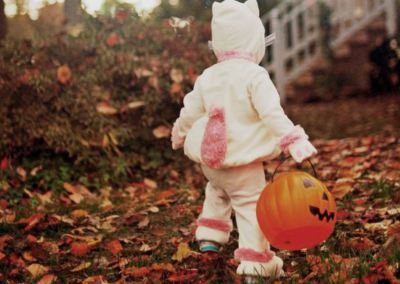 A little kid in a cat costume holding a plastic Jack-o'-lantern bin
